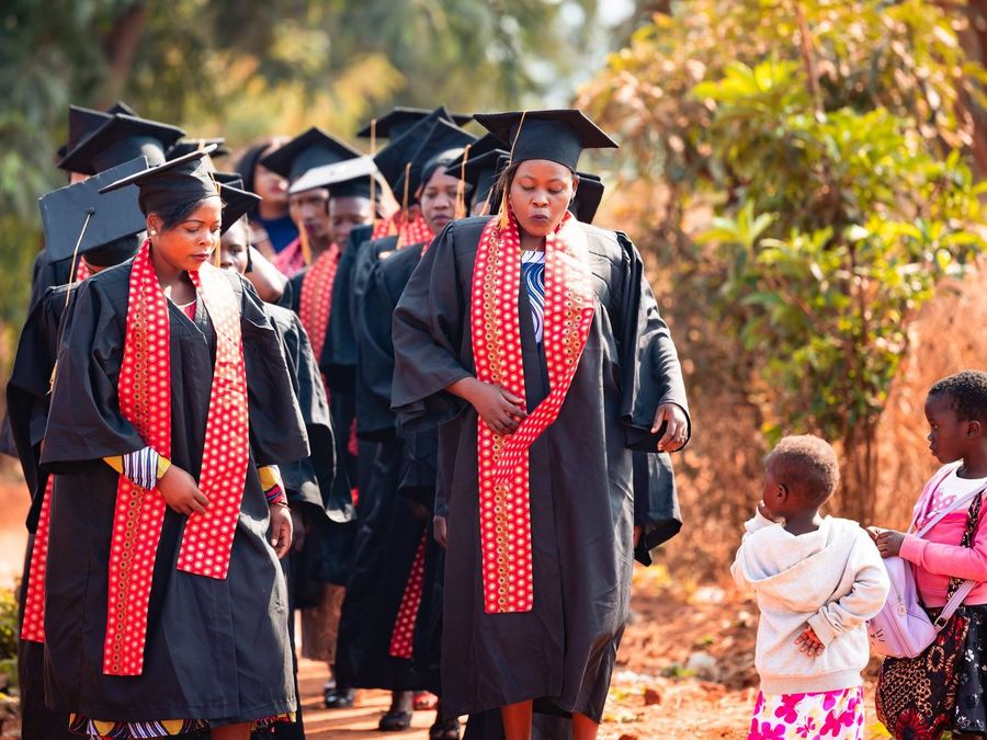 Graduates in caps and gowns walking with children in Chinsapo, Malawi